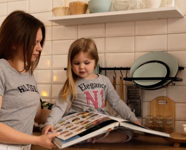 A mother and daughter enjoy reading a cookbook in a modern kitchen, sharing fun and learning together.