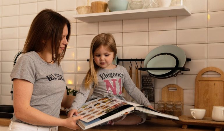 A mother and daughter enjoy reading a cookbook in a modern kitchen, sharing fun and learning together.