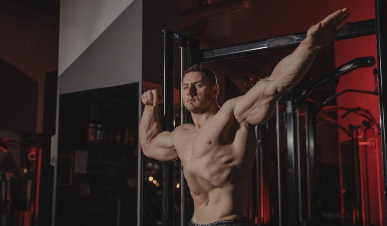 Strong and muscular man posing topless in a gym, showcasing fitness and strength.